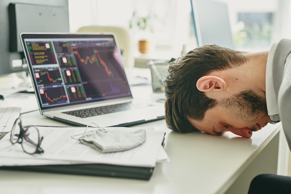 Frustrated young manager banging his head on table after financial analysis of company budget, failure in business during coronavirus